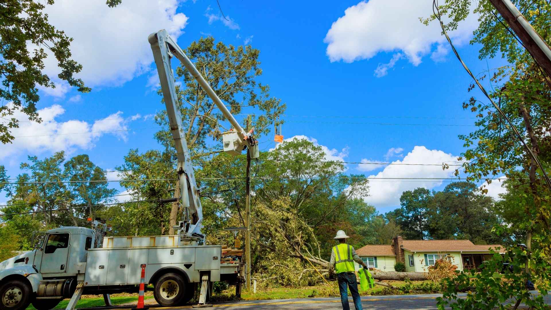 utility workers use a bucket truck to repair power lines after a fallen tree caused damage near a residential area.