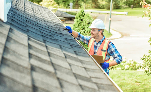 A man with hard hat standing on steps inspecting house roof.